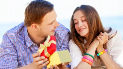 Ein Mann überreicht einer lächelnden Frau mit geschlossenen Augen und gefalteten Händen eine herzförmige Geschenkschachtel mit gelber Schleife - eine Szene voller Geschenkideen für Freundin: romantisch und kreativ.